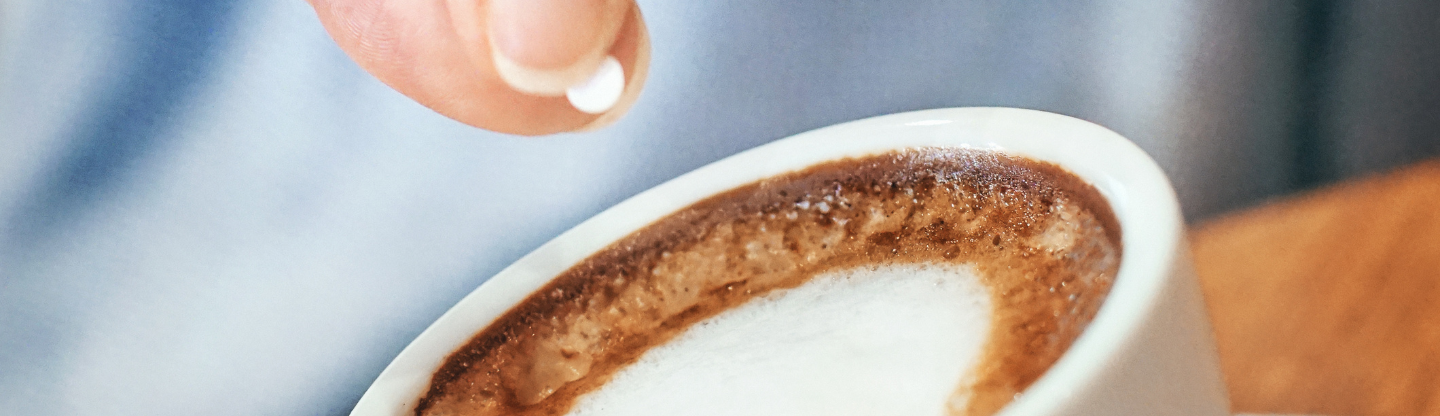 A person dropping a sweetener into a cup of coffee
