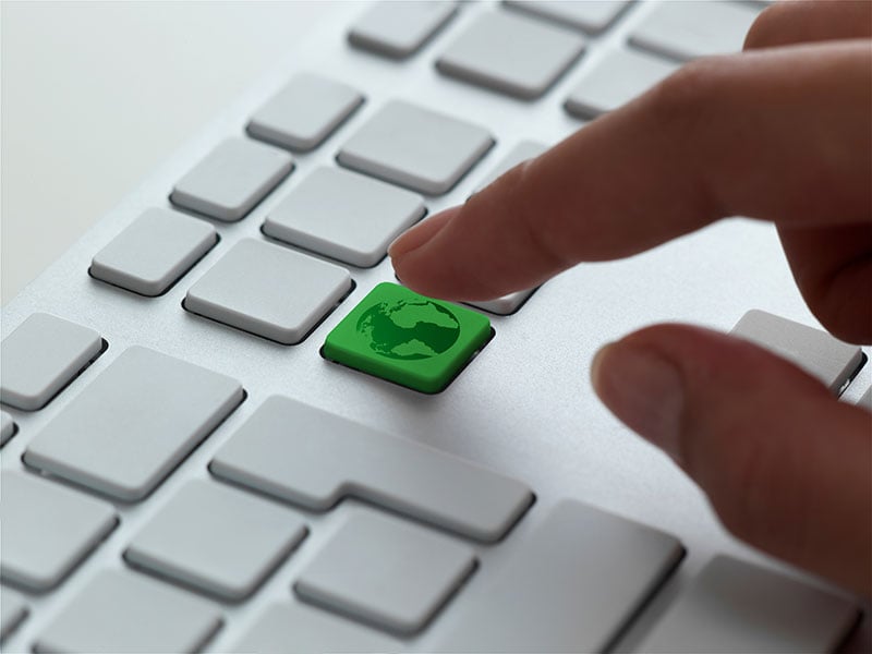 A finger pressing a green globe key on a keyboard