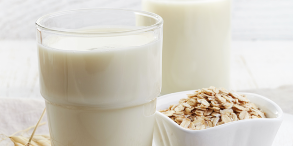 A glass of diary free milk alternative sits on a table top next to a bowl of healthy cereal