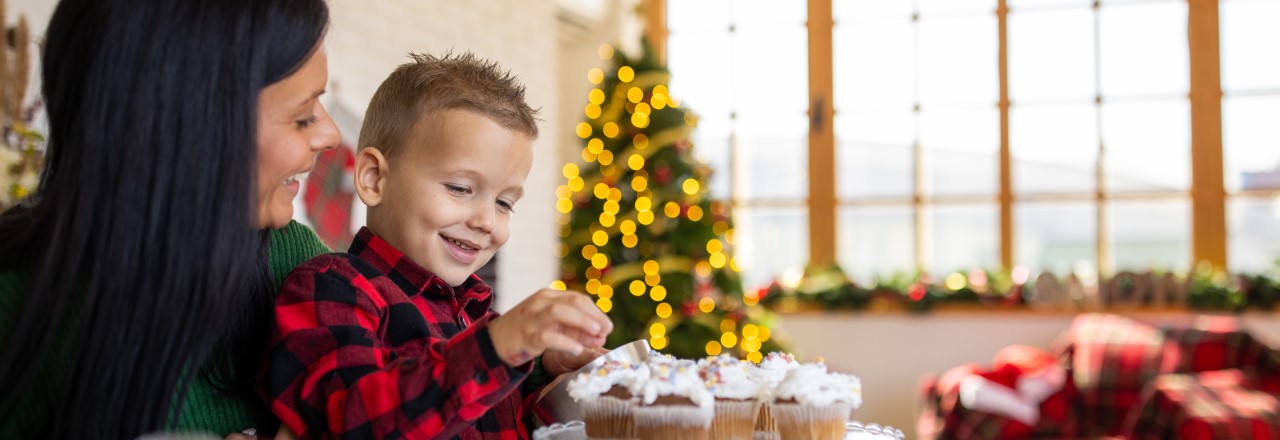 A young boy sits on his mothers lap while they decorate healthy holiday desserts recipes together.