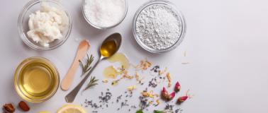 An assortment of products sit on a white table in glass jars surrounded by flower petals